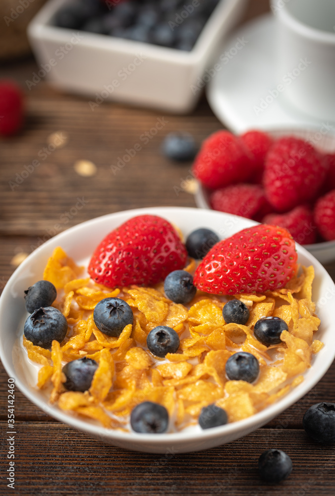 Corn flakes with blueberries and raspberries in white bowl in dark wooden desk. Corn flakes with blueberries and raspberries in white bowl in dark wooden desk.