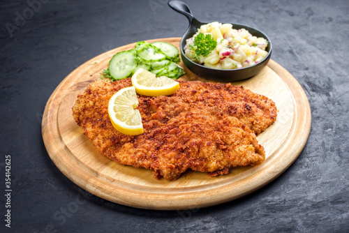 Traditionelles frittiertes Wiener Schnitzel mit Kartoffel und Gurken Salat angeboten als closeup auf einem rustikalen Holz Board