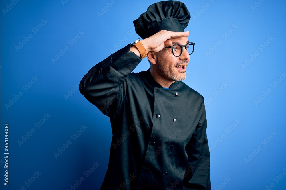 Young handsome chef man wearing cooker uniform and hat over isolated blue background very happy and smiling looking far away with hand over head. Searching concept. Young handsome chef man wearing cooker uniform and hat over isolated blue background very happy and smiling looking far away with hand over head. Searching concept.