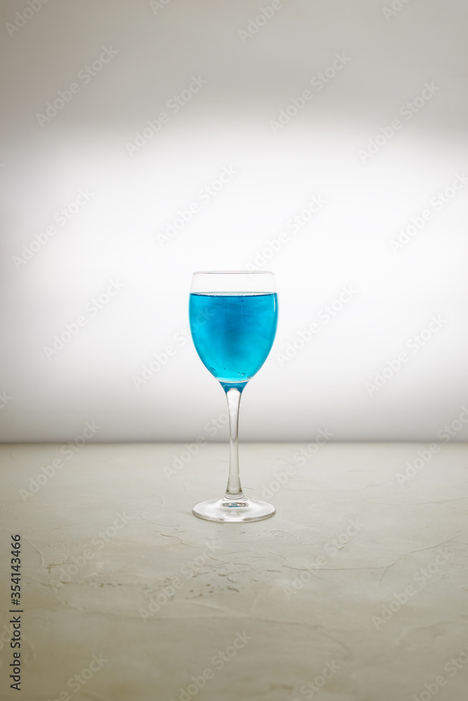 Fototapeta premium Glass of blue glitter drink on a light background. Sparkling blue wine.