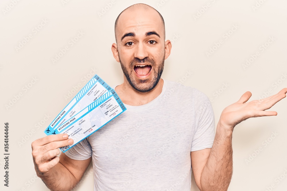 Young handsome bald man holding airline boarding pass celebrating achievement with happy smile and winner expression with raised hand Young handsome bald man holding airline boarding pass celebrating achievement with happy smile and winner expression with raised hand