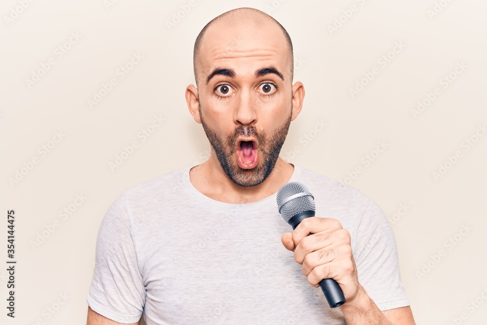Young handsome bald man singing song using microphone scared and amazed with open mouth for surprise, disbelief face Young handsome bald man singing song using microphone scared and amazed with open mouth for surprise, disbelief face