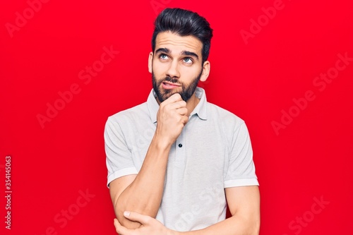 Young handsome man with beard wearing casual polo with hand on chin thinking about question, pensive expression. smiling with thoughtful face. doubt concept.