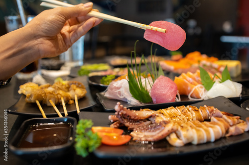 Hand holding tuna sashimi using chopsticks.