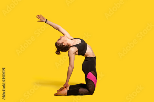 Camel pose. Athletic woman with hair bun in tight sportswear practicing yoga, doing spinal back bending ustrasana exercise with raised hand, stretching muscles. full length studio shot, sport workouts photo