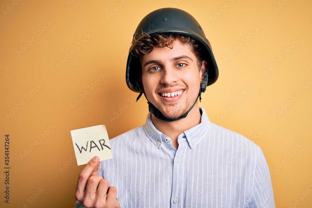 Young blond businessman with curly hair wearing helmet holding paper with war message with a happy face standing and smiling with a confident smile showing teeth Young blond businessman with curly hair wearing helmet holding paper with war message with a happy face standing and smiling with a confident smile showing teeth