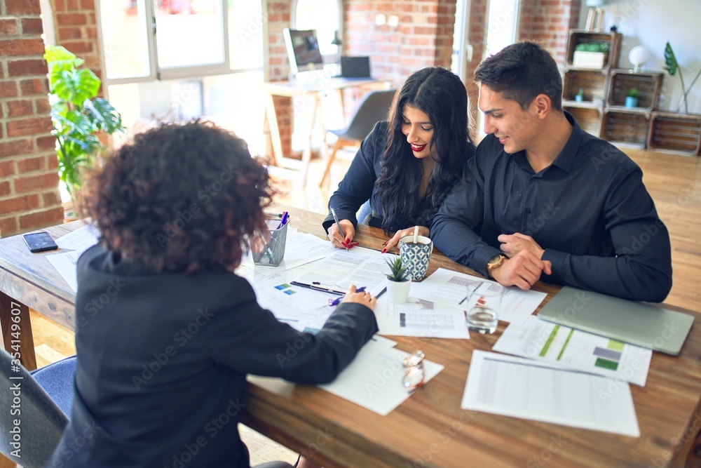 Young beautiful couple applying for mortgage. Sitting smiling happy meeting with real state agent signing mortgage loan at bank Young beautiful couple applying for mortgage. Sitting smiling happy meeting with real state agent signing mortgage loan at bank