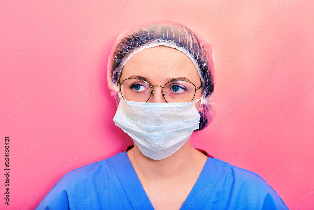 Portrait of a doctor woman with sad facial expression, close up. Nurse in a blue uniform and a medical mask on a pink background. Portrait of a doctor woman with sad facial expression, close up. Nurse in a blue uniform and a medical mask on a pink background.