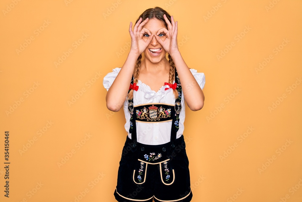 Young beautiful blonde german woman with blue eyes wearing traditional octoberfest dress doing ok gesture like binoculars sticking tongue out, eyes looking through fingers. Crazy expression. Young beautiful blonde german woman with blue eyes wearing traditional octoberfest dress doing ok gesture like binoculars sticking tongue out, eyes looking through fingers. Crazy expression.