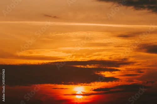Magical orange bright sunset with sunbeams and dark gloomy clouds. Twilight background  nightly dramatic wallpaper. Meteorology  weather forecast. Warm golden sky. Sun disk