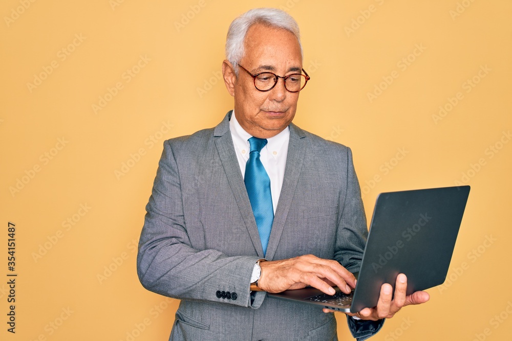 Middle age senior grey-haired business man wearing glasses working using computer laptop with a confident expression on smart face thinking serious Middle age senior grey-haired business man wearing glasses working using computer laptop with a confident expression on smart face thinking serious
