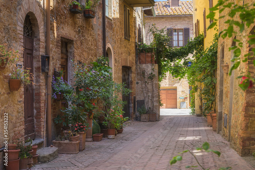 Fototapeta Naklejka Na Ścianę i Meble -  Sunny streets with colorful flowers with contrasting shades. Walk the Tuscan town