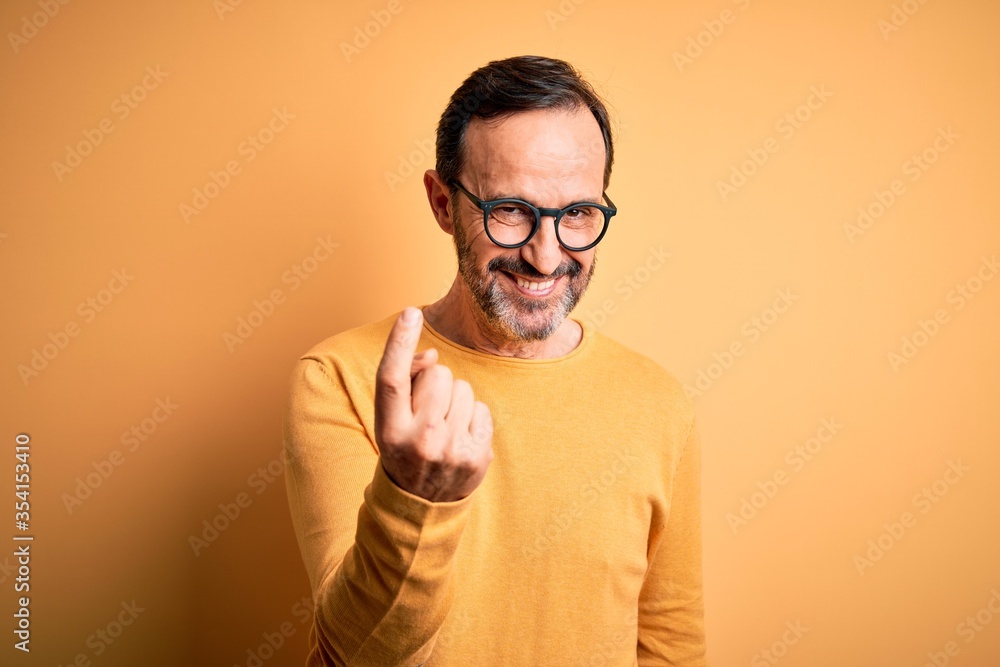 Middle age hoary man wearing casual sweater and glasses over isolated yellow background Beckoning come here gesture with hand inviting welcoming happy and smiling Middle age hoary man wearing casual sweater and glasses over isolated yellow background Beckoning come here gesture with hand inviting welcoming happy and smiling