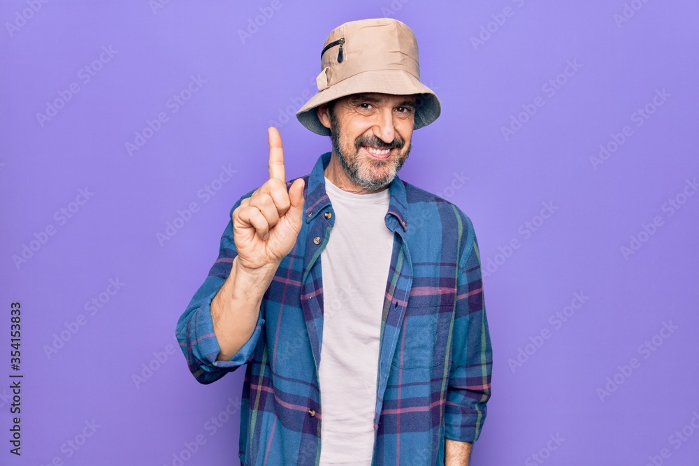 Middle age handsome man wearing casual shirt and hat over isolated purple background smiling with an idea or question pointing finger up with happy face, number one Middle age handsome man wearing casual shirt and hat over isolated purple background smiling with an idea or question pointing finger up with happy face, number one