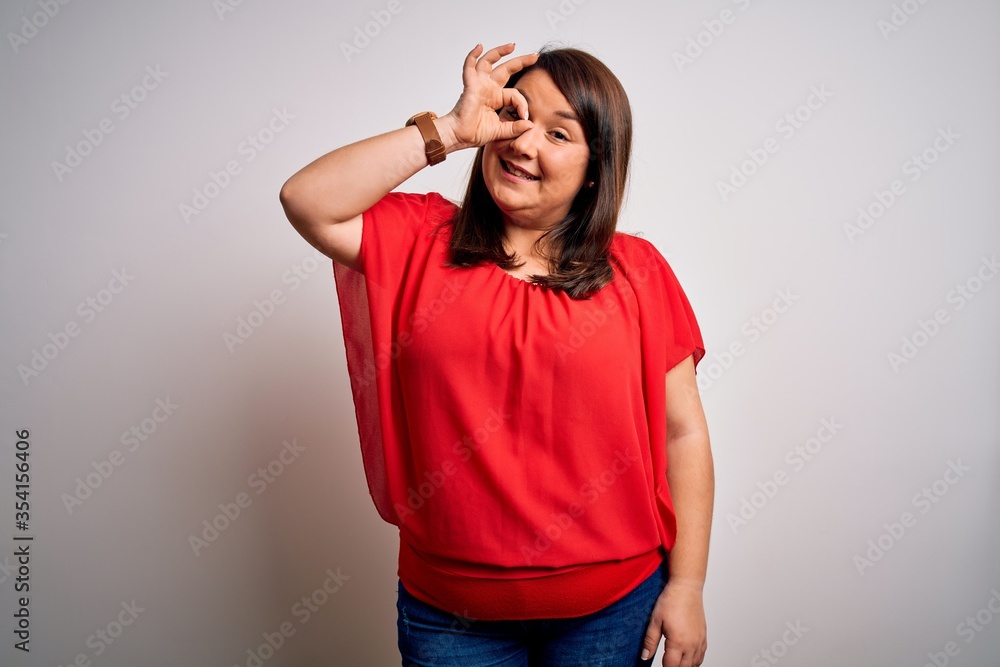 Beautiful brunette plus size woman wearing casual red t-shirt over isolated white background doing ok gesture with hand smiling, eye looking through fingers with happy face. Beautiful brunette plus size woman wearing casual red t-shirt over isolated white background doing ok gesture with hand smiling, eye looking through fingers with happy face.