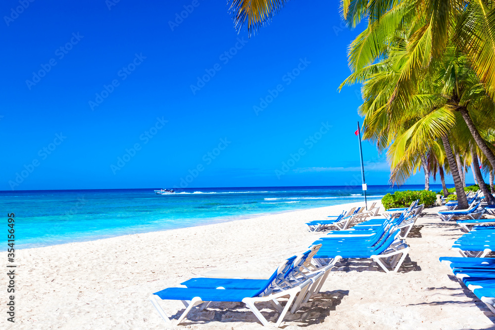 Beautiful tropical beach with sun loungers and palms. Saona Island, Dominican Republic. Caribbean resort. Vacation travel background.