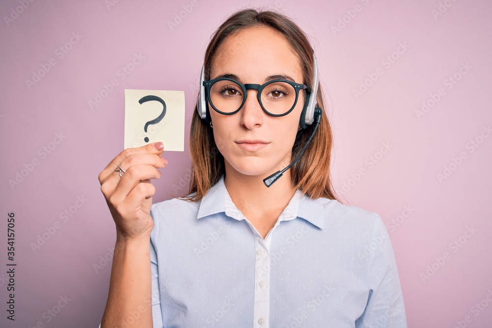 Beautiful call center agent woman working using headset holding reminder with question mark with a confident expression on smart face thinking serious Beautiful call center agent woman working using headset holding reminder with question mark with a confident expression on smart face thinking serious