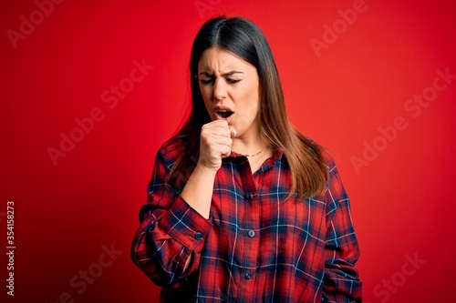 Young beautiful woman wearing casual shirt over red background feeling unwell and coughing as symptom for cold or bronchitis. Health care concept. © Krakenimages.com