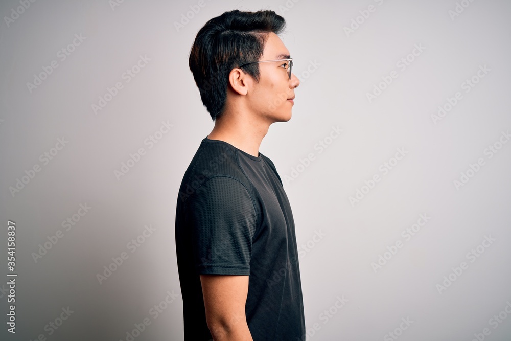 Obraz premium Young handsome chinese man wearing black t-shirt and glasses over white background looking to side, relax profile pose with natural face with confident smile.