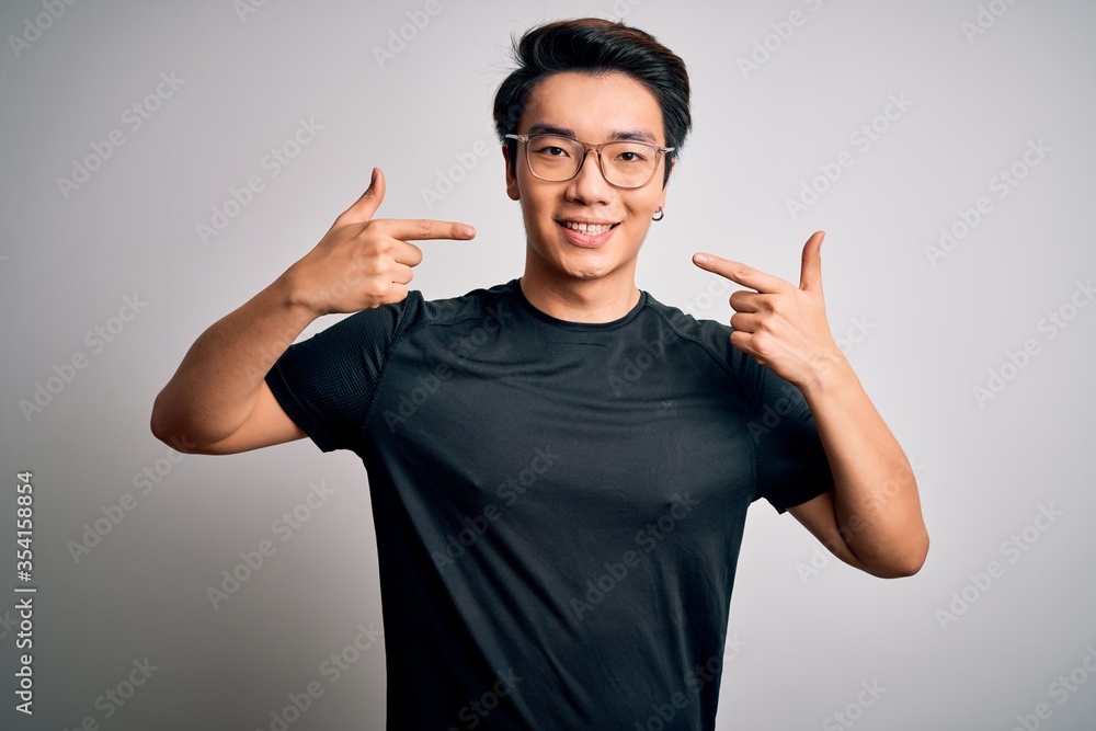 Young handsome chinese man wearing black t-shirt and glasses over white background smiling cheerful showing and pointing with fingers teeth and mouth. Dental health concept. Young handsome chinese man wearing black t-shirt and glasses over white background smiling cheerful showing and pointing with fingers teeth and mouth. Dental health concept.