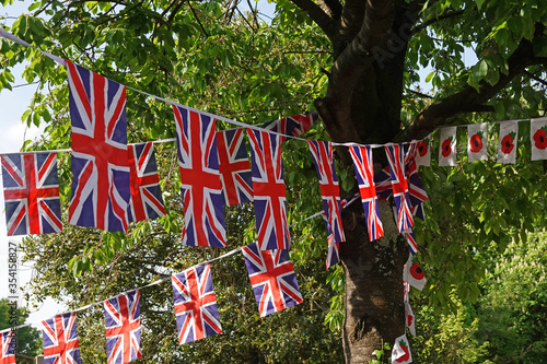 Union flag and poppy flag bunting hanging in the shade of a tree on a village green in the UK