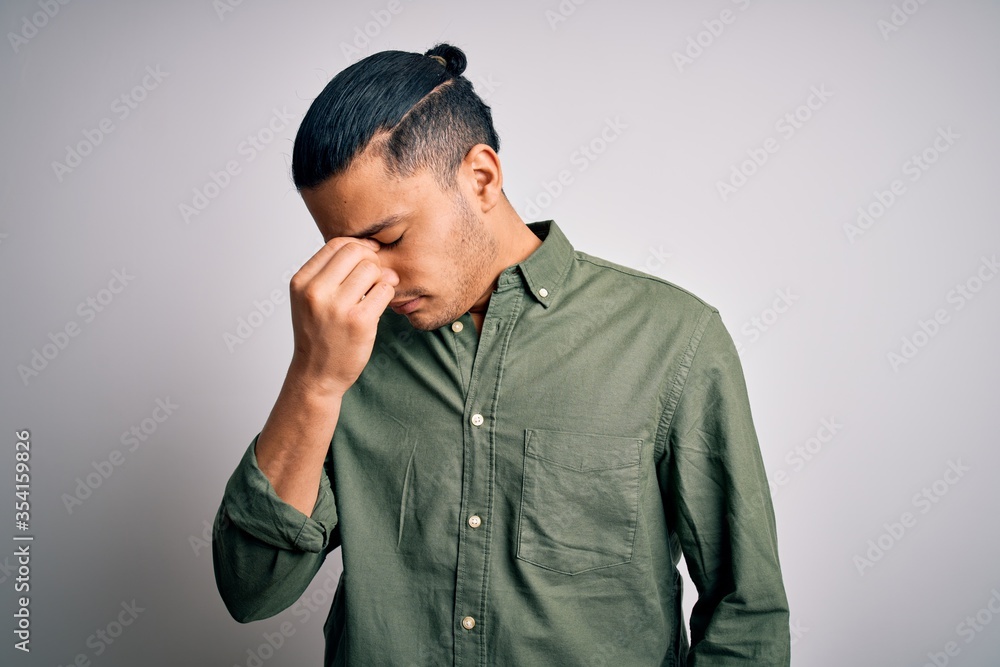 Young brazilian man wearing casual shirt standing over isolated white background tired rubbing nose and eyes feeling fatigue and headache. Stress and frustration concept. Young brazilian man wearing casual shirt standing over isolated white background tired rubbing nose and eyes feeling fatigue and headache. Stress and frustration concept.