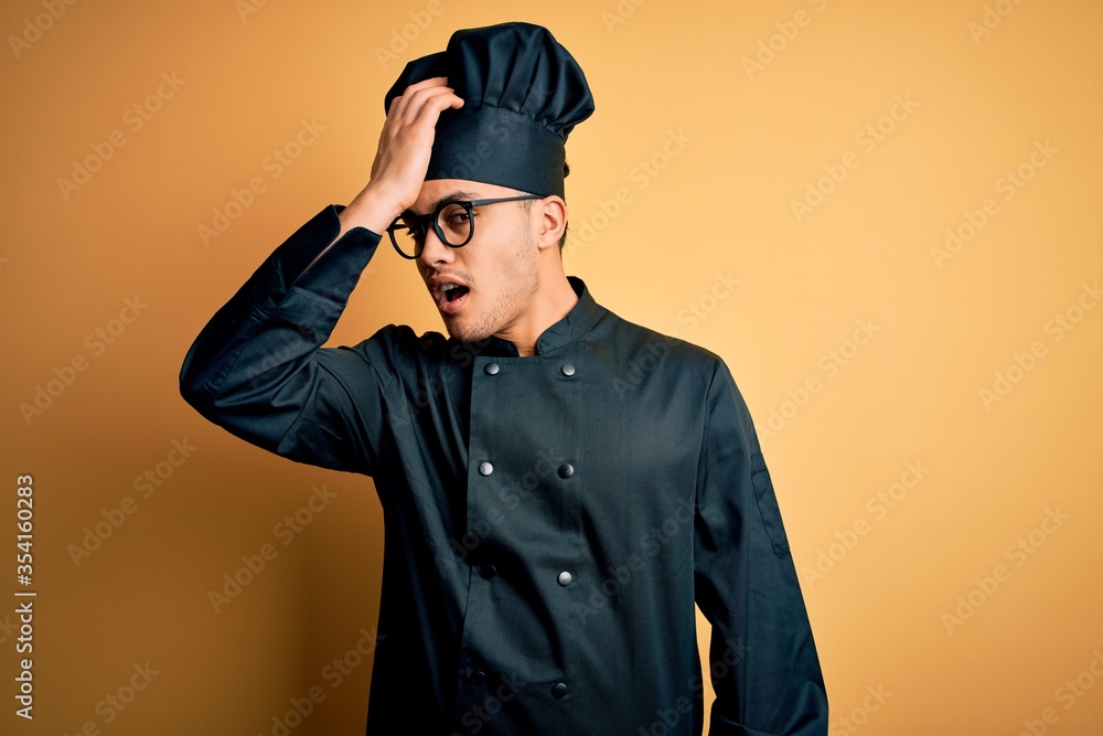 Young brazilian chef man wearing cooker uniform and hat over isolated yellow background surprised with hand on head for mistake, remember error. Forgot, bad memory concept. Young brazilian chef man wearing cooker uniform and hat over isolated yellow background surprised with hand on head for mistake, remember error. Forgot, bad memory concept.
