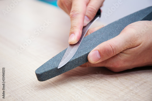 Strong male hands sharpen a kitchen metal knife with a grindstone. Home household knife sharpening.
