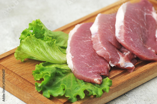 raw pork steak - pork neck - with lettuce leaves on a wooden Board