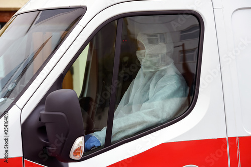 People with protective suits helping a sick man outdoors, coronavirus concept. Ambulance car.