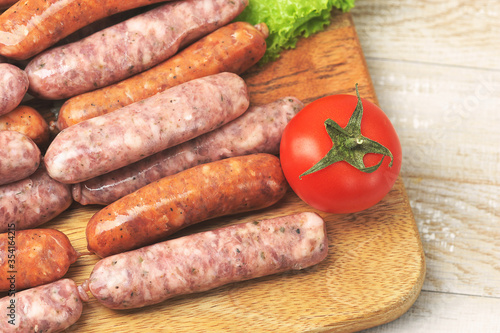 raw grilled sausages on a wooden round Board with tomatoes