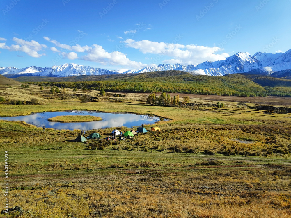 Altai, panoramic view of the lake and mountains against the background of the forest, a tent camp for tourists, autumn, blue sky.