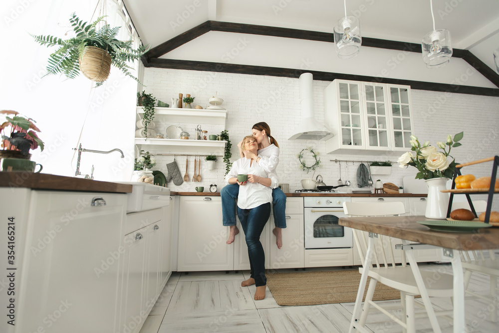 Happy elderly mother and daughter in the kitchen, they drink tea and enjoy a conversation. Old mother with an adult daughter at home Happy elderly mother and daughter in the kitchen, they drink tea and enjoy a conversation. Old mother with an adult daughter at home