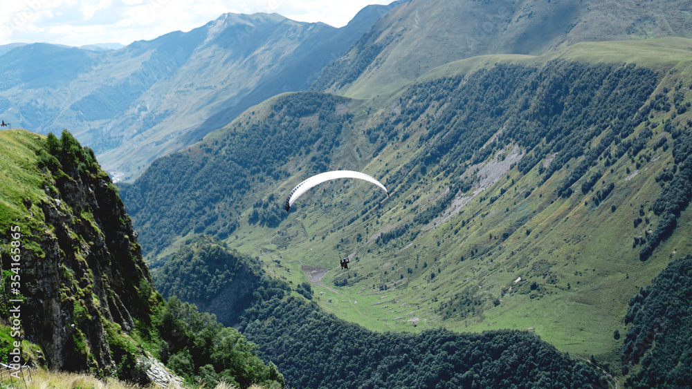 Paraglider flying over mountains during summer day - Georgia, kazbegi