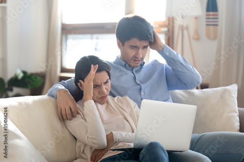 Frustrated young man and woman sit on sofa at home concerned by unpleasant unexpected news online, unhappy caucasian couple distressed with eviction email or notification, or having laptop problems