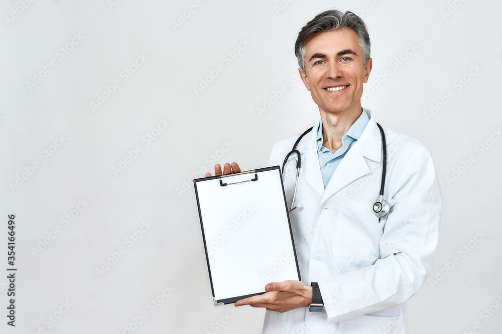 Portrait of happy mature doctor in medical uniform with stethoscope around neck showing folder with documents at camera while standing against grey background Portrait of happy mature doctor in medical uniform with stethoscope around neck showing folder with documents at camera while standing against grey background