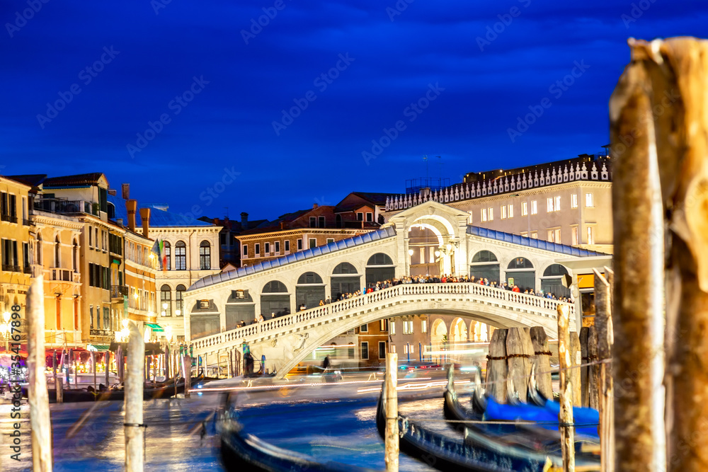 Rialto bridge and Grand Canal at twilight blue hour in Venice, Italy. Gondolas on the foreground. Tourism and travel concept.