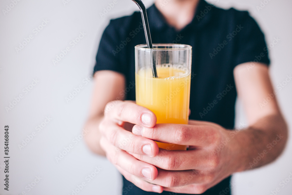 Young man isolated over background. Cut view of guy holding glass of juice with plastic straw in it. Defocused and blurred background. Young man isolated over background. Cut view of guy holding glass of juice with plastic straw in it. Defocused and blurred background.