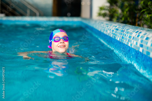 Happy girl in pink swimsuit with swimming hat and glasses in the blue pool in sportclub photo