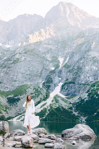 girl in white dress posing on the shore of a mountain lake. Rock © Ivan