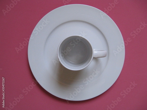 taza blanca honda tipo mug en centro de plato grande plano blanco de servir sobre fondo rosa. Vista cenital 