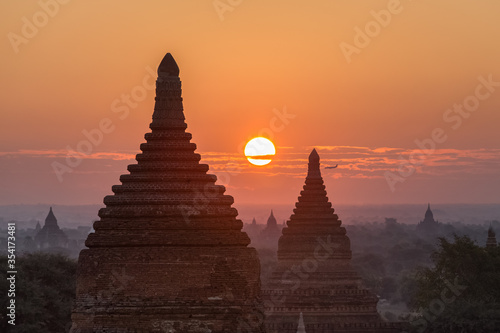 Sunrise over ancient pagodas in Bagan  Pagan   Myanmar  with a silhouette of descending plane on horizon. Bagan is an ancient city with thousands of buddhist temples and stupas