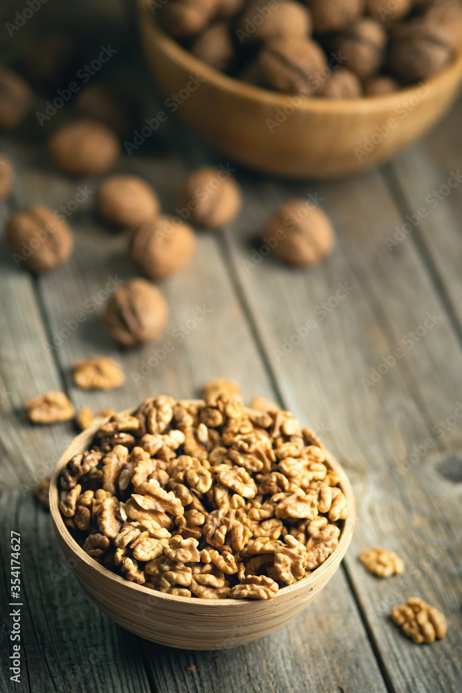 Fresh walnut kernels and whole walnuts in a bowl on rustic old wooden table. Healthy organic food, BIO viands, natural background. Copy space for your advertising text message Fresh walnut kernels and whole walnuts in a bowl on rustic old wooden table. Healthy organic food, BIO viands, natural background. Copy space for your advertising text message