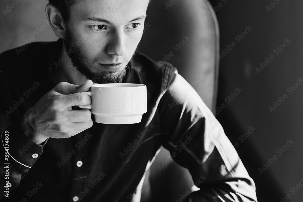 good looking man drinking coffee on the armchair on black and wh good looking man drinking coffee on the armchair on black and wh