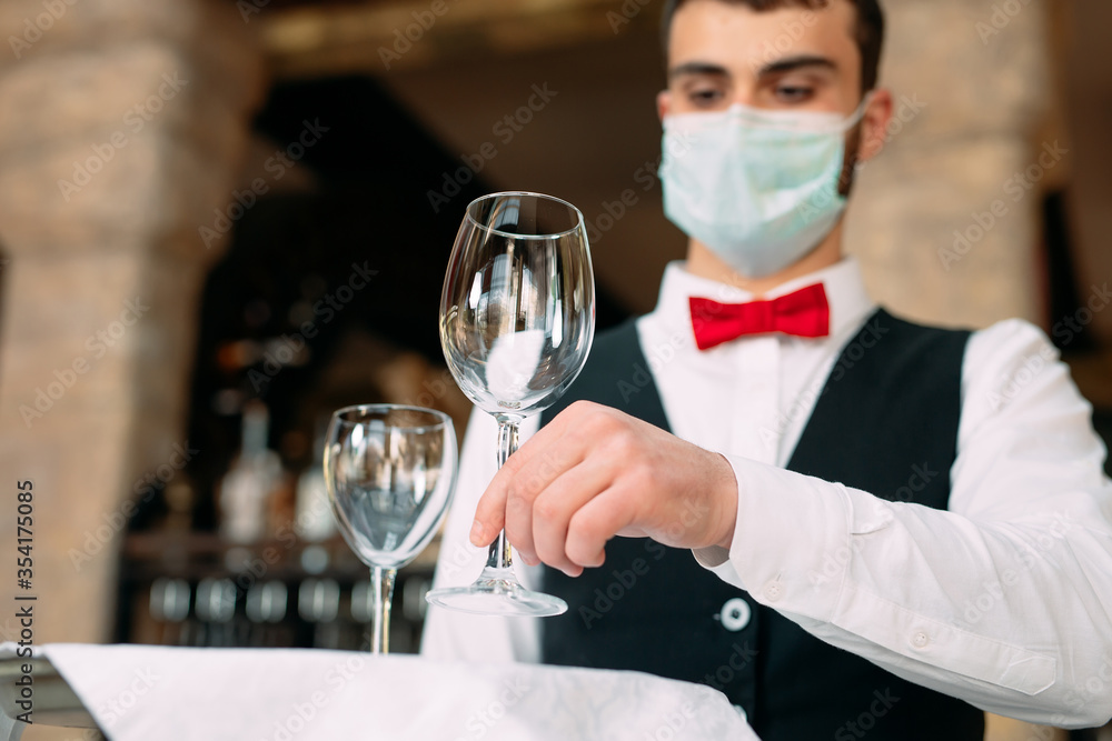 A waiter in a medical protective mask serves the table in the restaurant. A waiter in a medical protective mask serves the table in the restaurant.