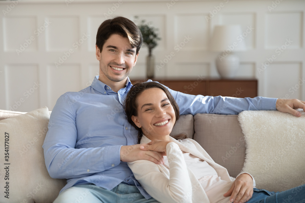 Portrait of smiling young man and woman sit relax n sofa at home hugging and cuddling, happy millennial caucasian couple rest on couch embracing, enjoy tender romantic weekend indoors together Portrait of smiling young man and woman sit relax n sofa at home hugging and cuddling, happy millennial caucasian couple rest on couch embracing, enjoy tender romantic weekend indoors together
