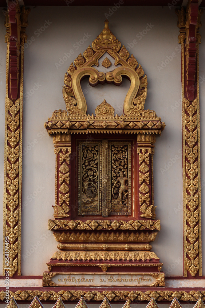 Decorative window with wood carving blinds and golden ornamental frame in a temple in Siamese Lao PDR, Southeast Asia