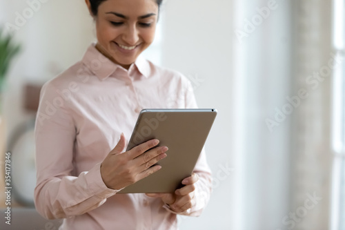 Focus on smiling millennial indian woman holding digital tablet, looking at screen. Pleasant happy hindu young businesswoman receive message with good news, working online, using electronic device.