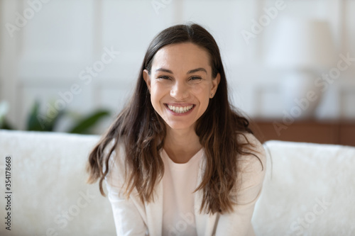 Headshot portrait of smiling millennial girl sit on sofa at home talk speak on web call, happy young caucasian woman engaged in online webcam conversation, have fun chat on dating service application