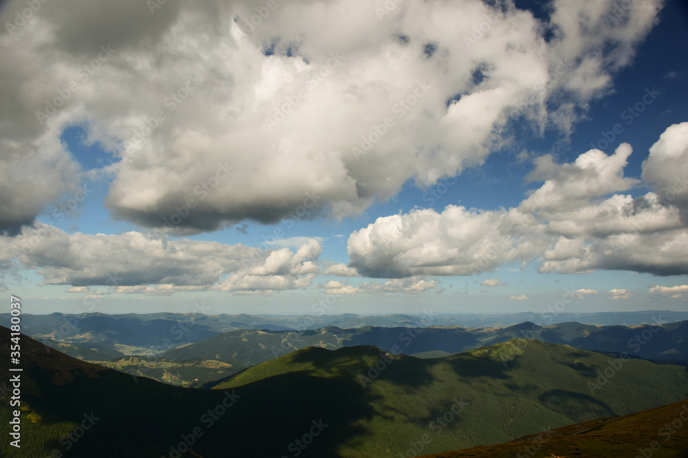 View of the valley from the top of the mountain on a background of several mountains and the sky with clouds